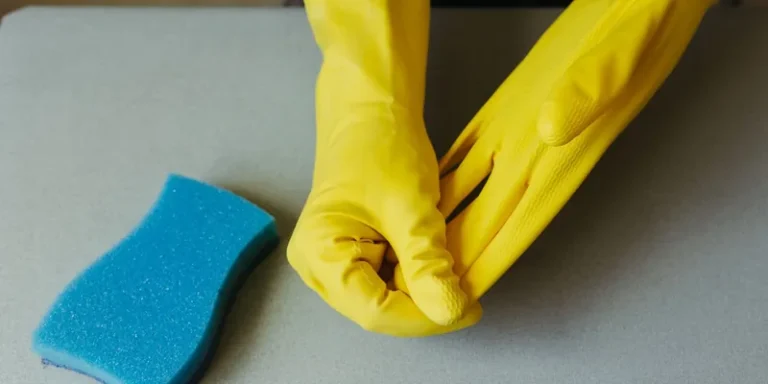 Persoon trekt gele rubberen handschoenen aan, schoonmaakspons op tafel