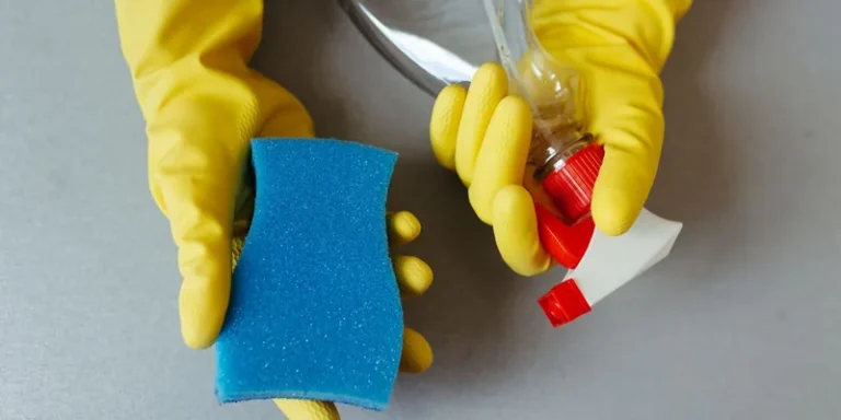 Handen in gele rubberhandschoenen met spons en spuitfles