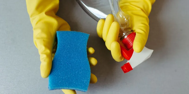 Handen in gele rubberhandschoenen met spons en spuitfles
